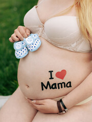 Pregnant woman in underwear holds children's shoes in her hands and has a sticker on her belly