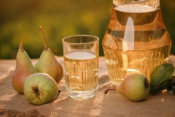 A glass with pear juice and basket with pears on wooden table with natural orchard background on sunset light. Vegetarian fruit composition