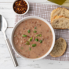 Bean soup in a bowl with bread slices and seasoning over wooden table