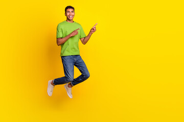 Fototapeta na wymiar Full length portrait of active cheerful person jumping indicate fingers empty space isolated on yellow color background
