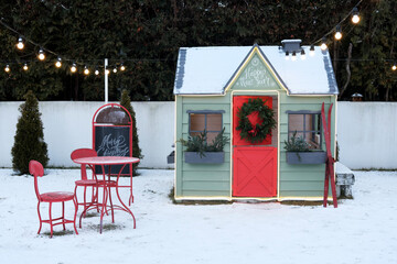 Cute wooden painted red-green private children play house in home garden, decorated with Christmas...