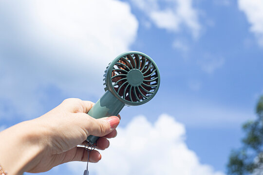 Mini portable blue electric fan. Hand holding bunny look like electric fan in blue cloudy background.