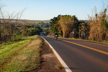 Ipaussu, São Paulo  Brazil - 09 23 2022: Highway illuminated by sunrise with a biker passing through 