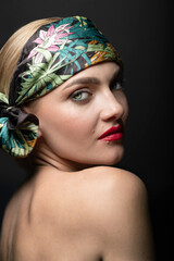 Fashion, style and make-up concept. Studio portrait of beautiful and sexy woman with red lipstick, green eyes and colorful scarf on her head. Model looking at camera through shoulder and naked back