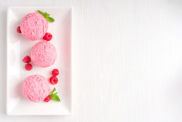 Top view of three scoops of berry frozen organic homemade ice cream or healthy sorbet served on plate decorated with raspberries and fresh mint leaf on white wooden background. Image with copy space - obrazy, fototapety, plakaty