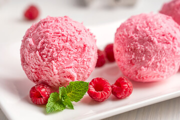 Close up view of scoop of berry frozen organic ice cream or healthy homemade sorbet of pink colour served on plate decorated with juicy sweet raspberries and mint leaves used as refreshing dessert
