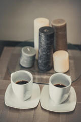 Two white cups of hot aromatic coffee on a brown table with candles. Composition in brown and beige tones.