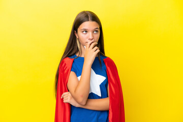 Little caucasian superhero girl isolated on yellow background having doubts and with confuse face expression