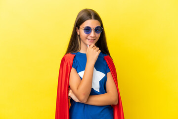 Little caucasian superhero girl isolated on yellow background with glasses and smiling