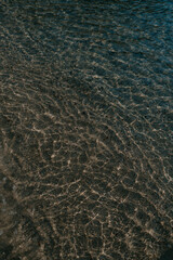 A relaxing scene of sun glistening in turquoise and emerald blue water in Rhodes, Greece. Rocks, waves, reflections, greenery, beach, sand