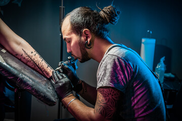Portrait of man tattoo master with dreadlocks showing process of creation tattoo on female body...