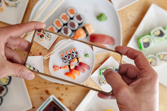Blogger with mobile phone taking photo of delicious sushi on table, top view