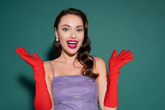 charming and excited woman in red gloves gesturing during celebration on green.