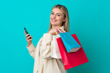 Young caucasian woman isolated on blue background holding shopping bags and writing a message with her cell phone to a friend