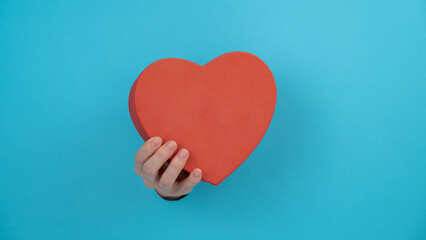A woman's hand with a heart-shaped gift box sticks out of a blue paper background. 