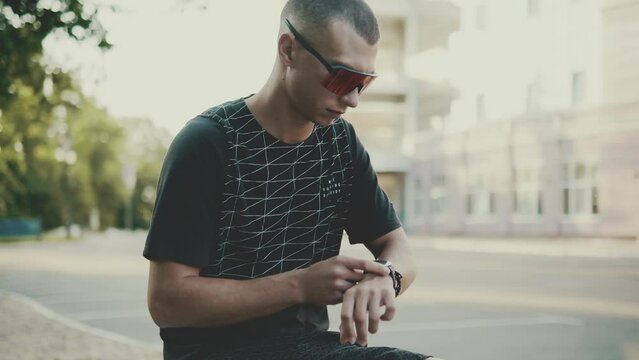 Serious sportsman adjusts the time on a wristwatch in the park outdoors