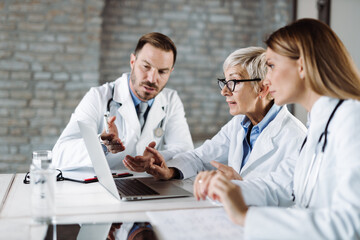 Group of doctors cooperating while working on laptop in a hospital