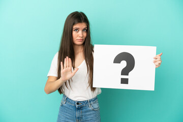 Young caucasian woman isolated on blue background holding a placard with question mark symbol and doing stop sign