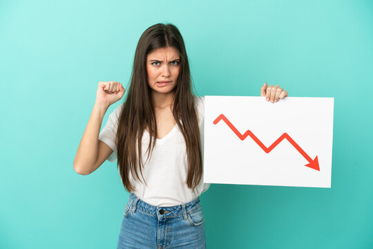 Young caucasian woman isolated on blue background holding a sign with a decreasing statistics arrow symbol and angry