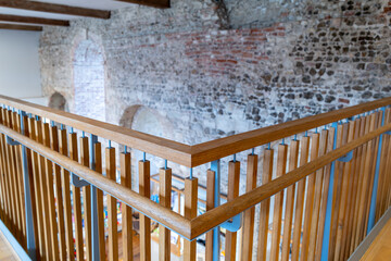 Newly installed wooden bannister and railings seen at the top of a medieval building in the UK. The old flint wall can be seen in the background.