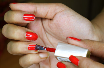 Woman putting red colour nail polish on her nails.