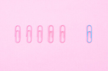 Pink colored aper clips arranged in a row. Blue paper clip standing out from the others.