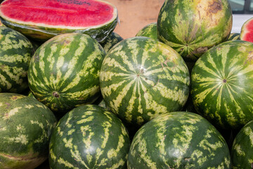 Many fresh and ripe watermelons lie on the counter in the market. Sale of watermelons at the farmers market. Close-up.Sale of ripe and fresh vegetables and fruits at the farmers' market.