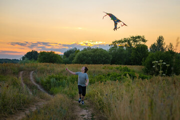 A teenager launches a kite at sunset in the summer in a field. The concept of hobbies, recreation and entertainment.