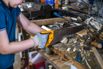 A teenager works using a saw in a garage and workshop.