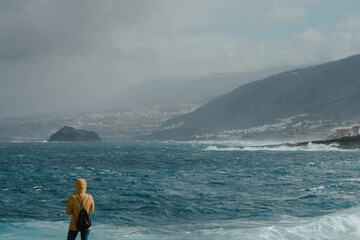 Woman with yellow jacket looking the fierce ocean and waiting the storm