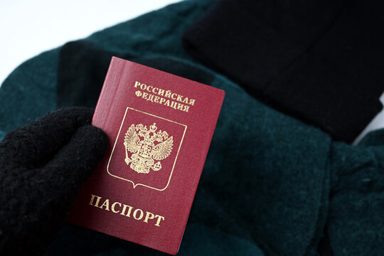Gloved hand holding a Russian passport with scarf and hat in the background. Winter travel, fleeing mobilization, official document