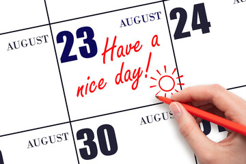 The hand writing the text Have a nice day and drawing the sun on the calendar date August 23