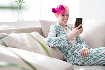 Young woman with colored pink and white hairs has video call using smart phone from home