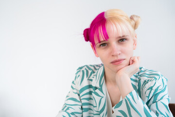 young blonde woman with pink hair sits at table with her chin in her hand isolated on white background