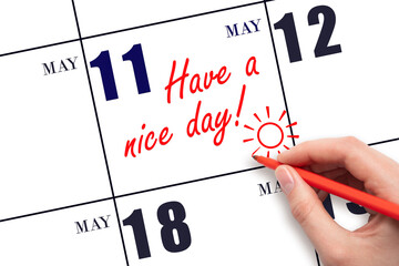 The hand writing the text Have a nice day and drawing the sun on the calendar date May 11