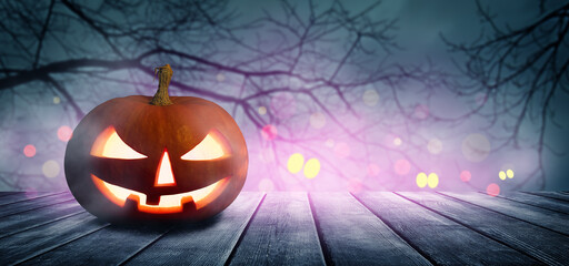 Two spooky Halloween pumpkins, Jack O Lantern, with an evil faces and eyes on a wooden table with a misty gray background.