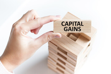 Capital Gains text on a wooden bar in a man's hand on a light background, a business concept