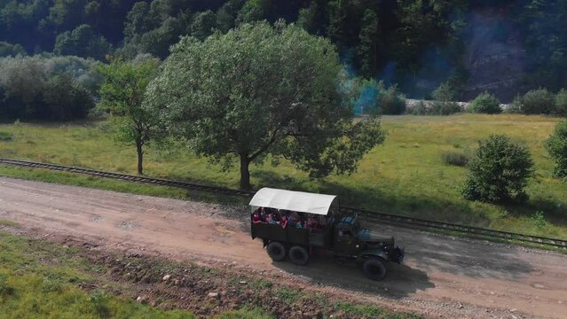 The truck is traveling along a mountain road on tourist route. A tourist trip through Ukrainian Carpathians in the summer. Big green tourist car Zil. Rest in nature among the river and green forests.