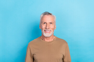 Photo of good mood optimistic senior man with gray hairstyle stubble wear beige t-shirt look empty space isolated on blue color background