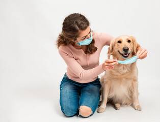 Female woman in medical protected face mask disinfects dogs paws with a sanitizer. A dog smile looks at camera with mask isolated on white background. Pets hygiene concept