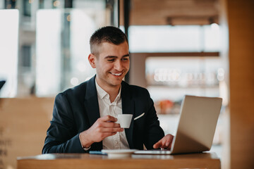 Happy business man sitting at cafeteria with laptop and smartphone
