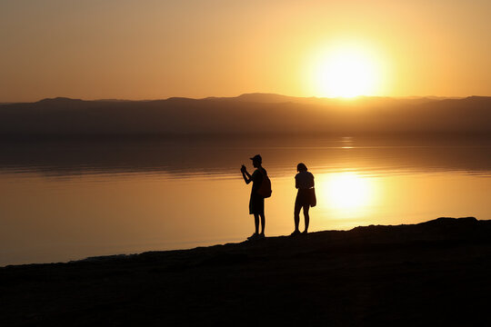 silhouette of couple photographing sunset on dead sea shore