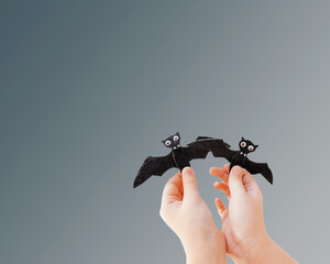 childs hands holding two model bats, gray background halloween