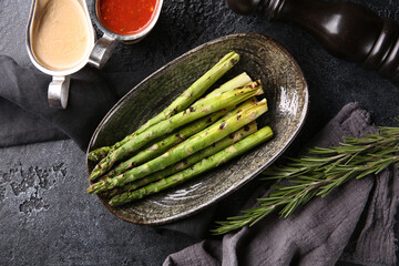 Grilled vegetables. Fried asparagus with herbs on a plate, red and white sauces, ketchup, spices. Rosemary on a dark table. Turkish cuisine, dish. Vegetable garnish. Background image, copy space