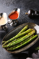 Grilled vegetables. Fried asparagus with herbs on a plate, red and white sauces, ketchup, spices. Rosemary on a dark table. Turkish cuisine, dish. Vegetable garnish. Background image, copy space