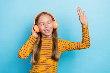 Portrait of excited carefree girl closed eyes hand touch headphones enjoy melody isolated on blue...