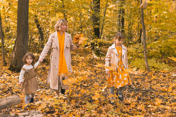 Young mother with her little daughters in an autumn park. Fall season, parenting and children concept.