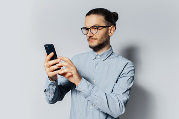 Studio portrait of young man using smartphone on white background, wearing blue shirt and eyeglasses.