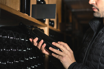 Man in the wine cellar with bottles in background drinking and tasting wine.