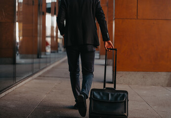 Going to airport terminal. Confident businessman traveler walking on city streets and pulling his...